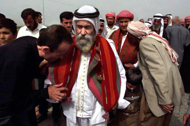 'Parade of the Sanjak': A sacred ancient brass peacock lamp representing Tawûsê Melek is carefully wrapped in wool fabric and carried in procession by a mir as Yezidi laity offer their respects.